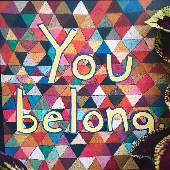 a sign that says you belong surrounded by plants